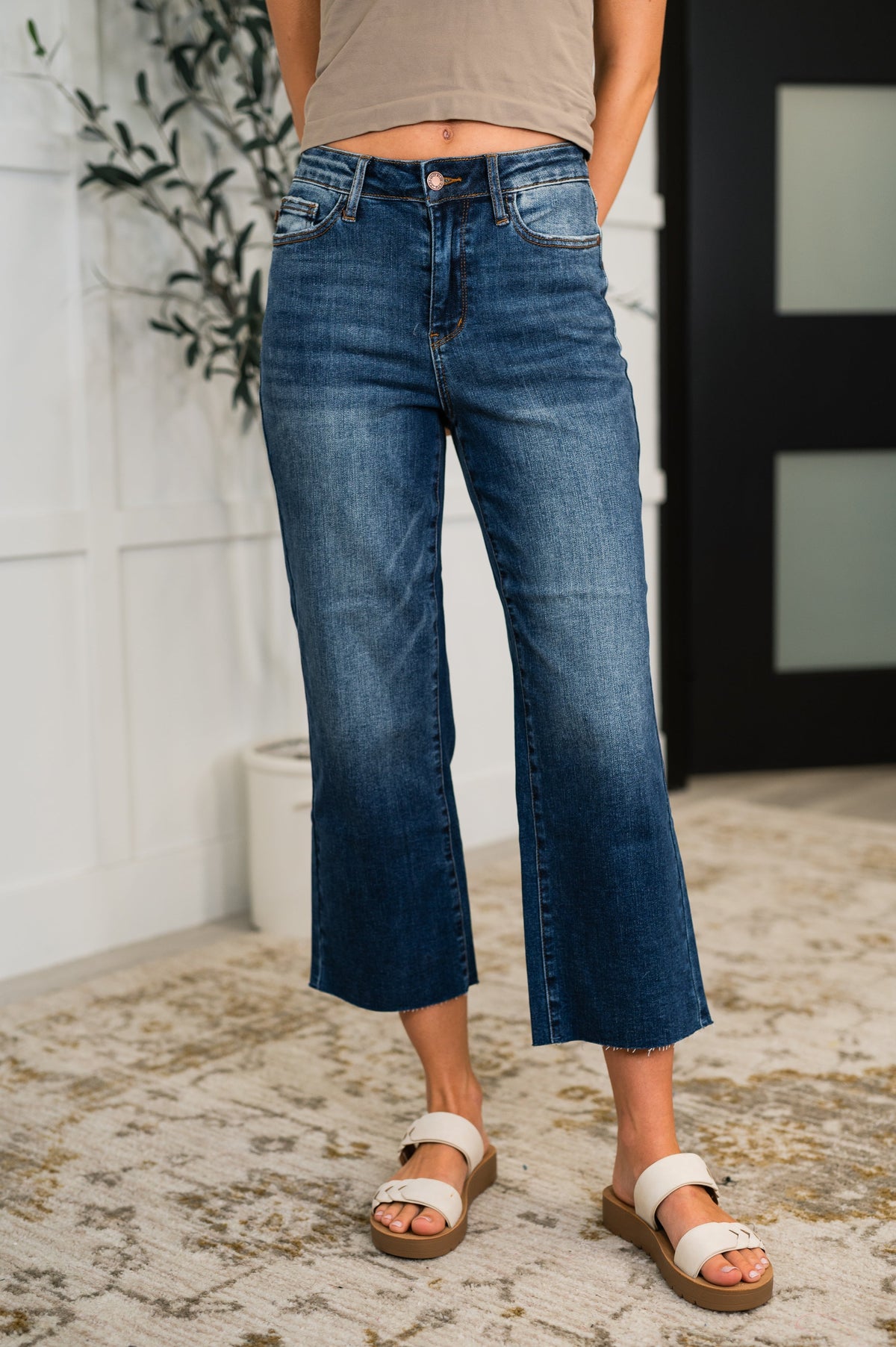 Woman wearing blue jeans and white sandals standing indoors.