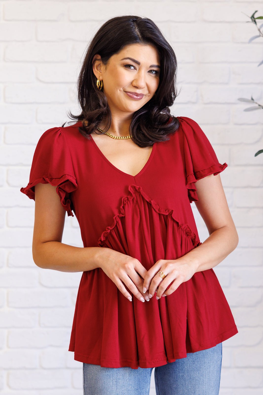 Woman wearing a red shirt with ruffled details against a white brick wall.