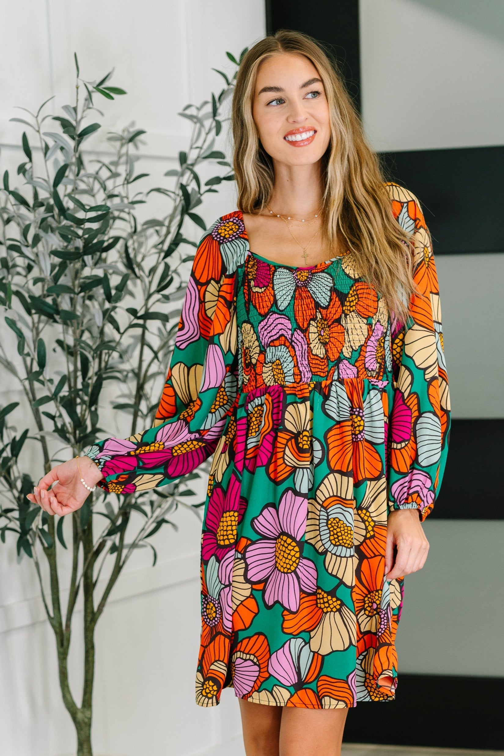 Woman wearing a colorful floral dress standing indoors with a plant in the background