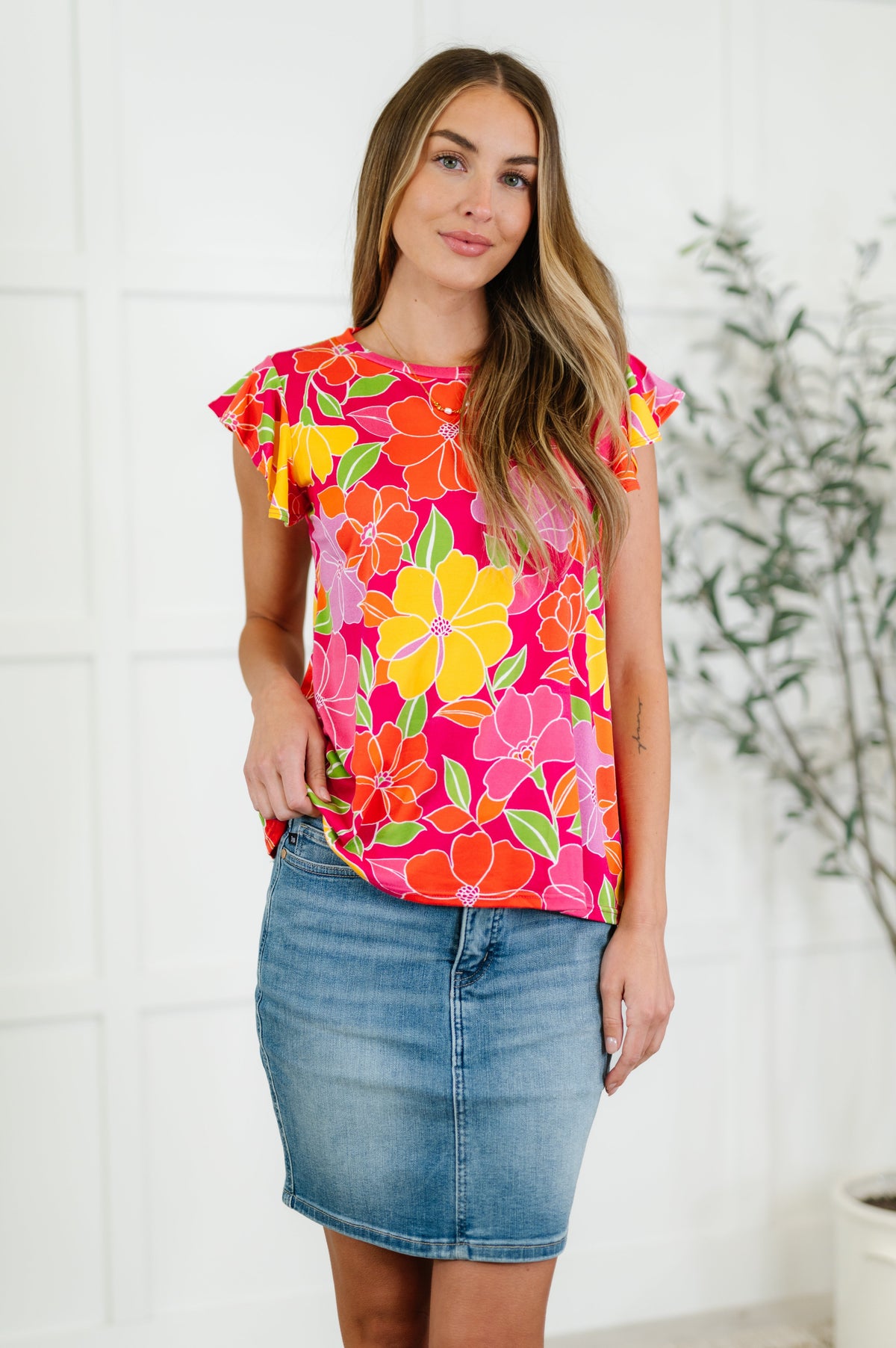 A woman wearing a colorful floral flutter sleeve top with a round neckline, paired with a blue denim skirt.