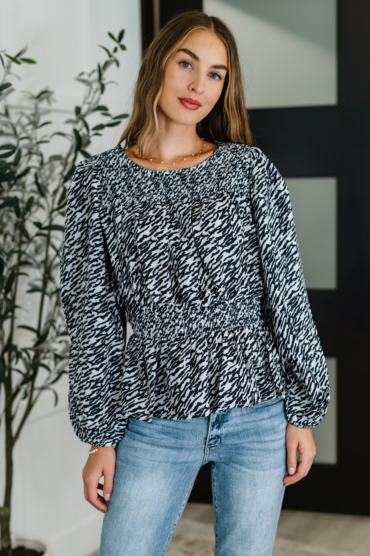 Woman wearing a black and white patterned blouse and blue jeans indoors.