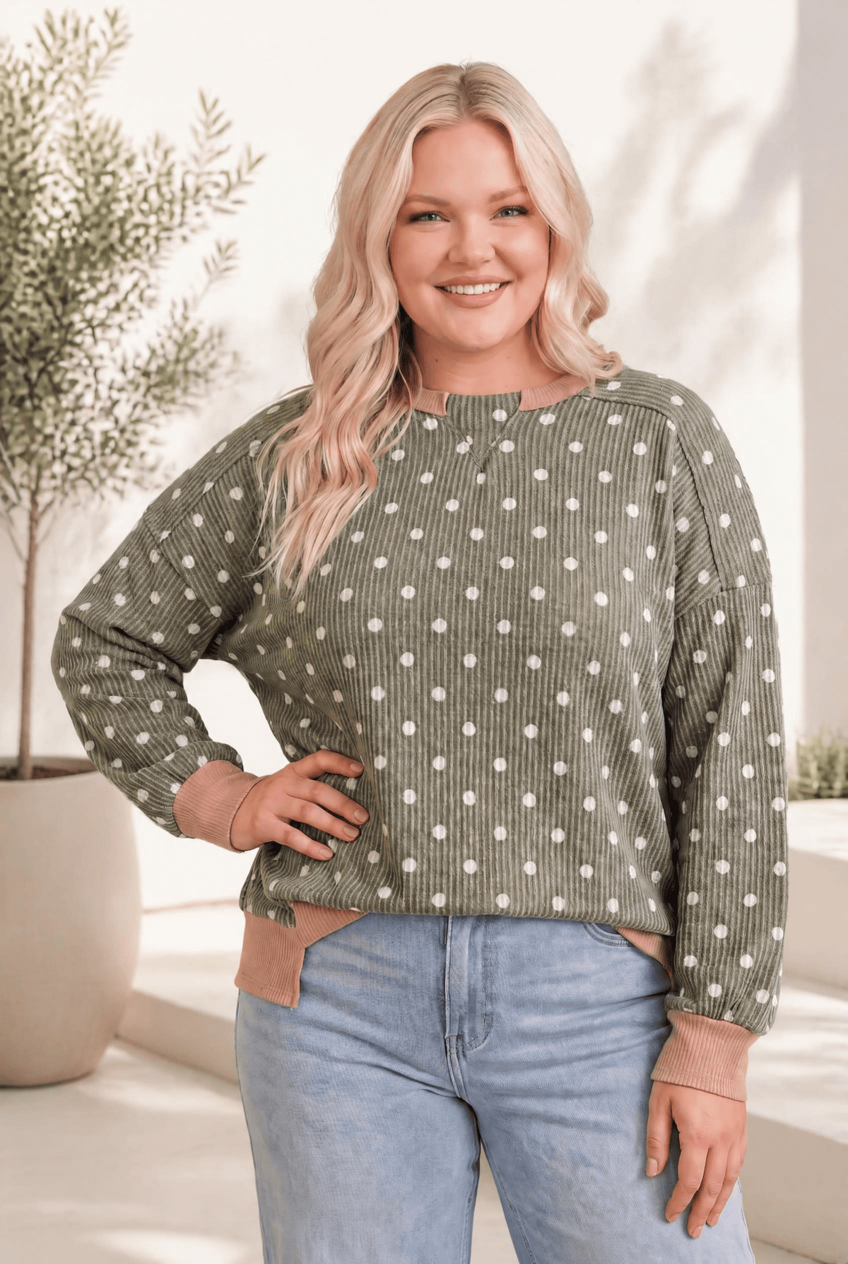 A cozy ribbed pullover in olive with white polka dots, mauve trim, and a relaxed fit, worn by a smiling model.