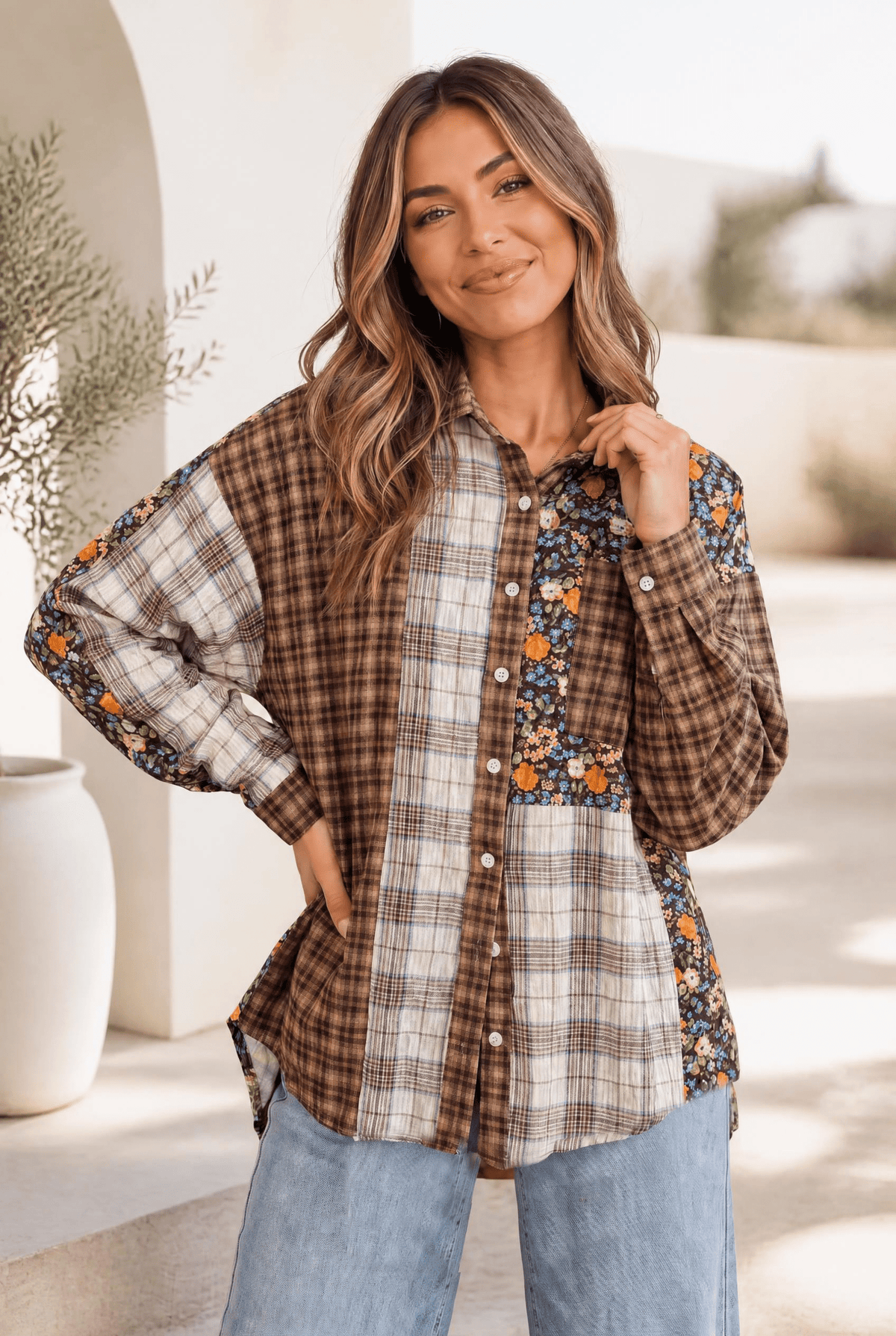 A mixed media button-down shirt with a plaid and floral patchwork design, shown on a model against a cozy backdrop.