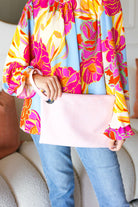 woman wearing a colorful floral blouse holding a pink clutch.