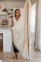 A large beige acrylic blanket with a textured pattern, held up by a person in a cozy room.