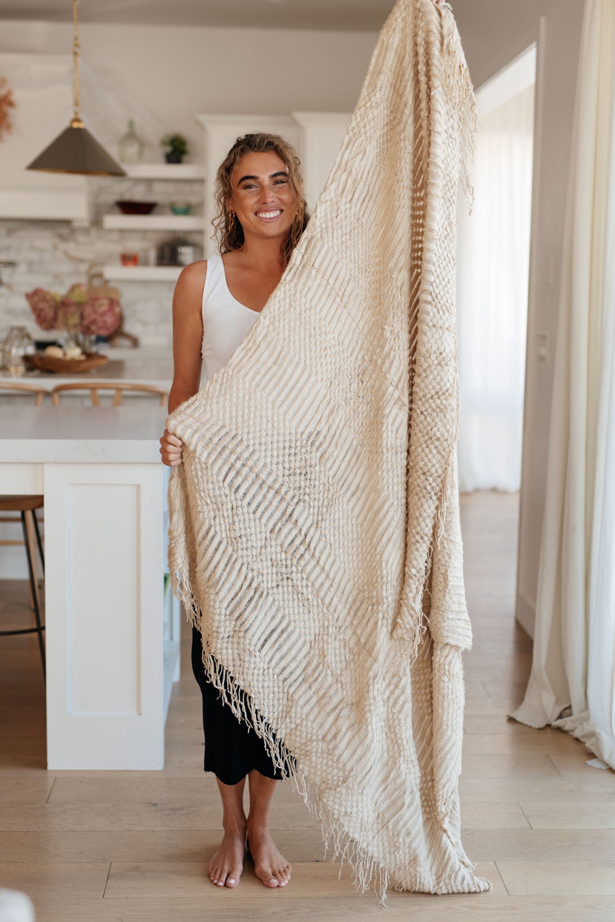 A large beige acrylic blanket with a textured pattern, held up by a person in a cozy room.