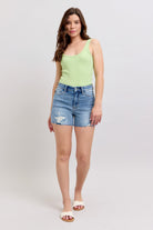 A Woman wearing a green tank top and blue distressed high-rise cutoff denim shorts with a raw hem.