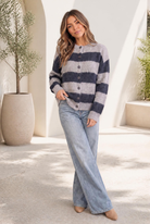 A woman wearing a fuzzy oversized cardigan with navy and grey wide stripes, buttoned front, and ribbed cuffs and hem.