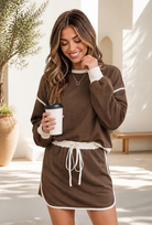 A woman wearing a mocha brown sweatshirt and mini skort set with cream contrast trim, holding a coffee cup.