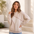 Woman wearing a sand-colored hoodie with contrast stitching and ribbed cuffs.