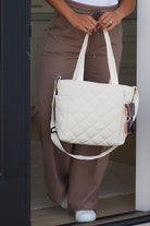 Cream quilted tote bag with adjustable straps and zipper closure.