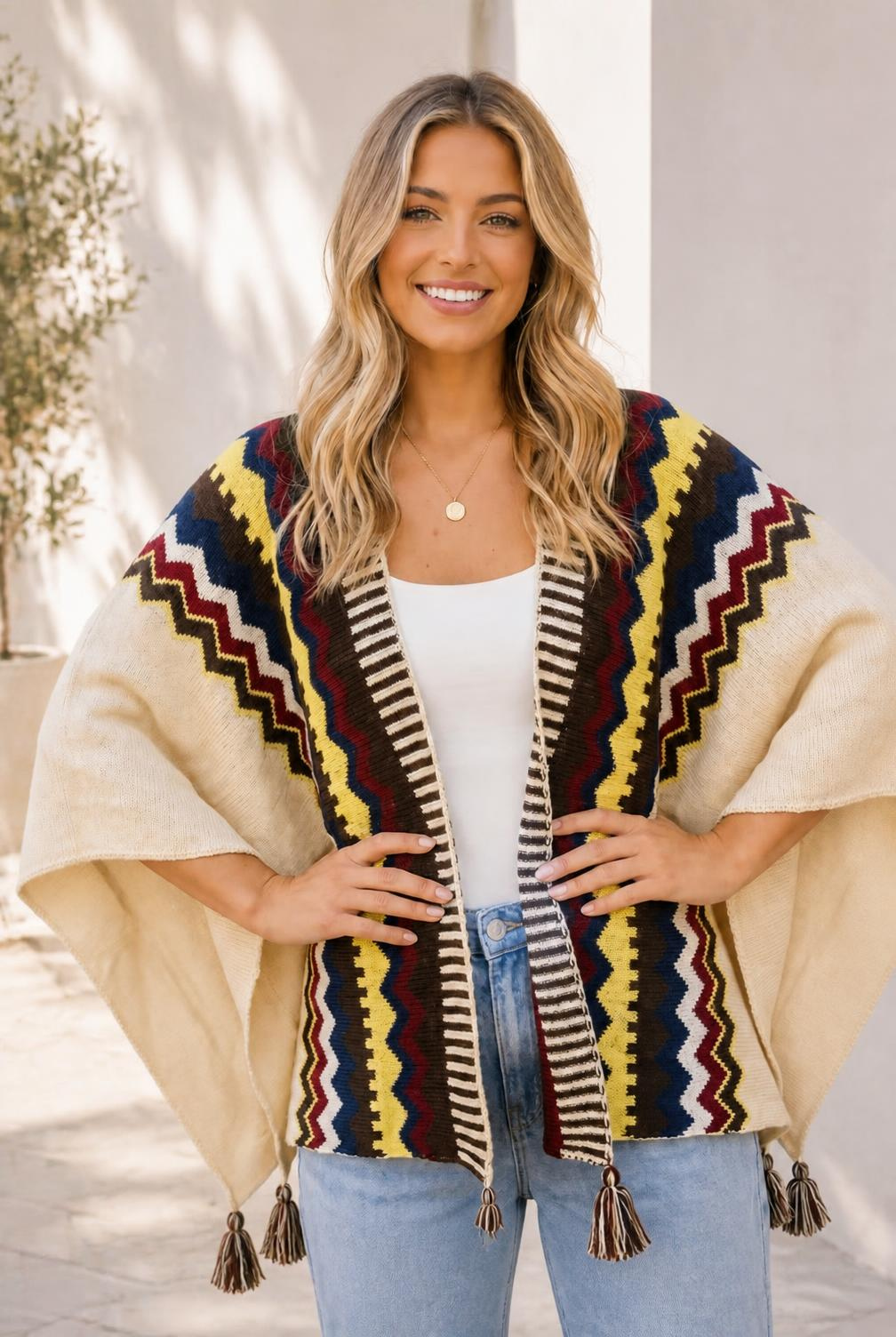 A woman wearing a cream knit wrap with multicolor chevron stripes and tassel details.