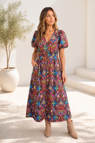 A woman wearing a chocolate brown midi dress with a colorful floral pattern and puff sleeves.
