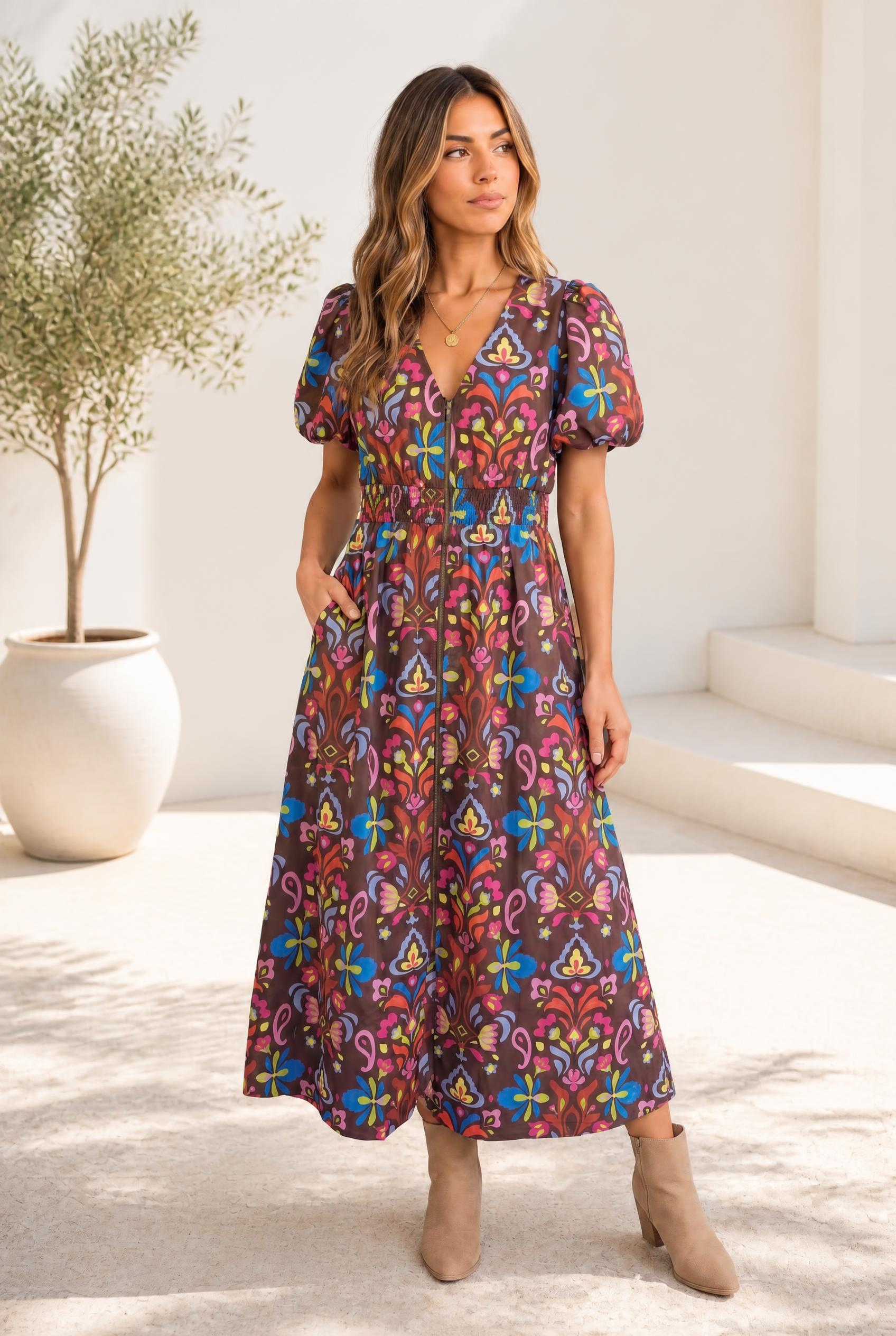 A woman wearing a chocolate brown midi dress with a colorful floral pattern and puff sleeves.
