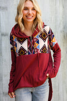 Woman wearing a colorful patterned hoodie with a red base against a wooden background