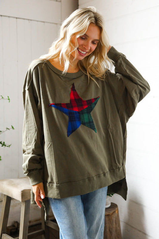 Woman wearing an olive green sweatshirt with a colorful star design, standing indoors.