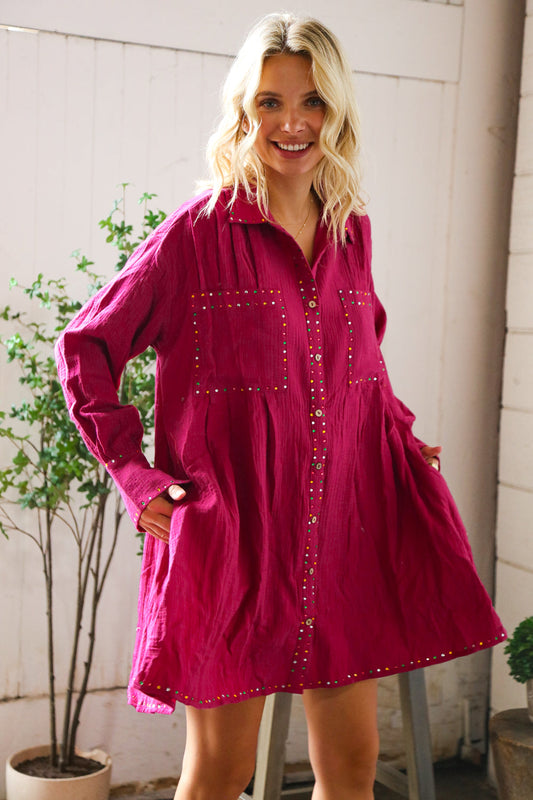 Woman wearing a pink dress with decorative buttons in an outdoor setting.