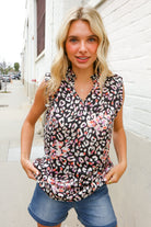 Woman wearing a sleeveless animal print top and denim shorts standing against a white wall.