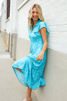 Woman wearing a blue dress leaning against a white wall.