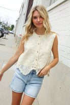 Woman wearing a white lace top vest and denim shorts on a city street.