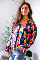 Woman wearing a colorful floral blouse with a white wall and plants in the background