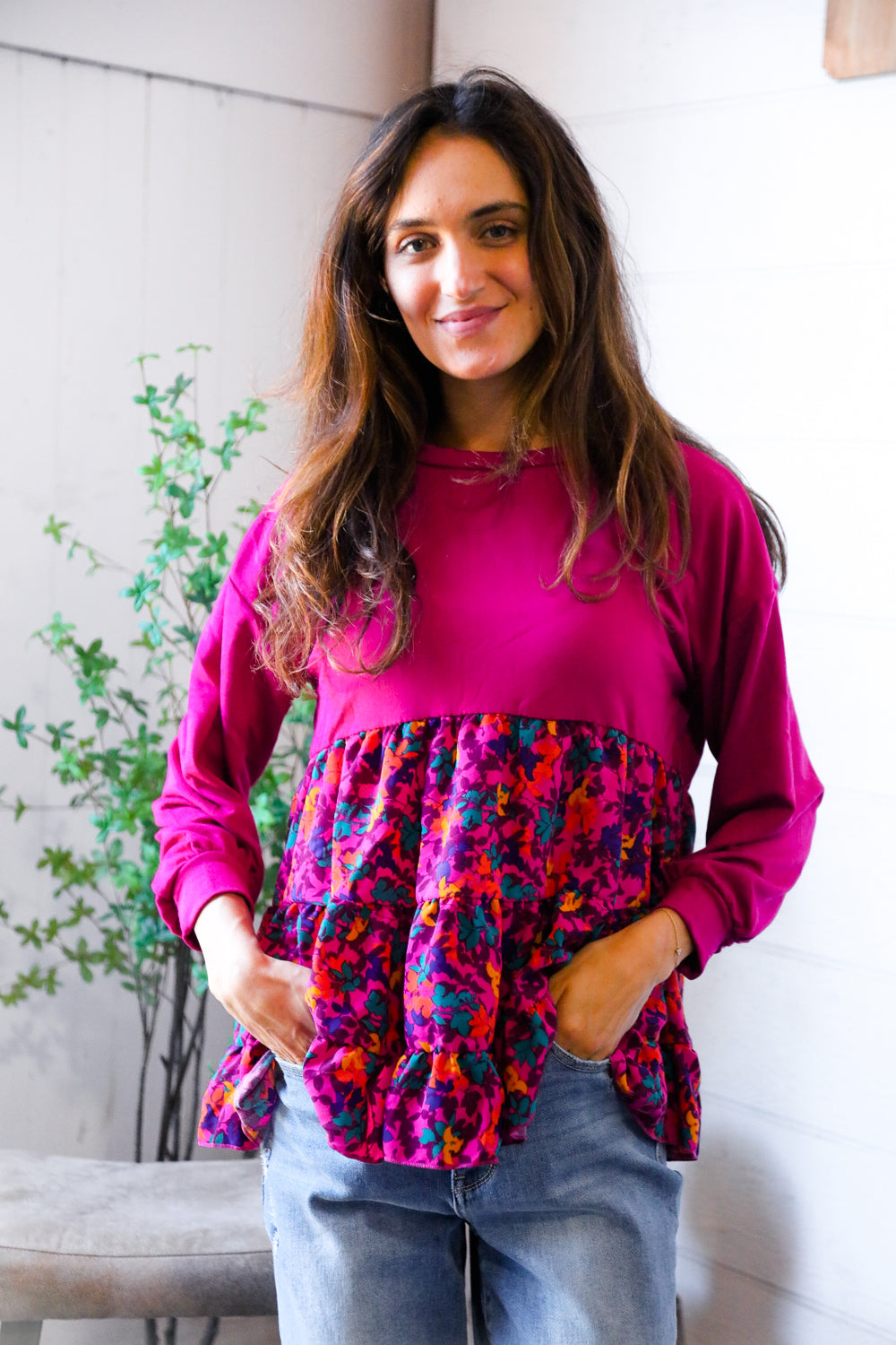 Woman wearing a pink top with a colorful floral pattern sitting indoors.