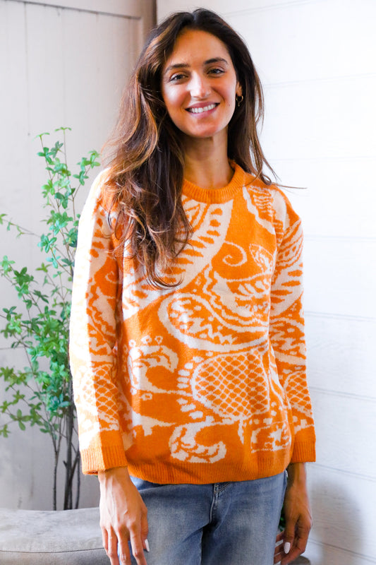 Woman wearing an orange sweater with a white pattern, standing indoors.