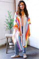 Woman wearing a colorful kimono-style garment indoors with a plant and bench in the background.