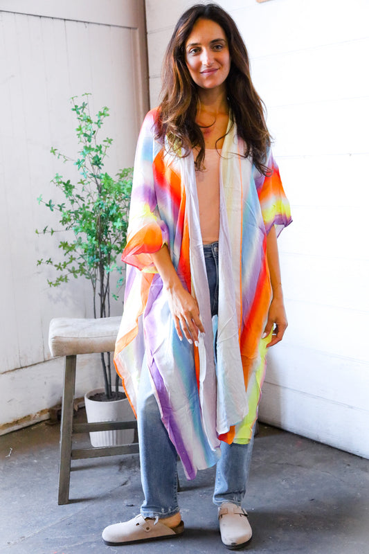 Woman wearing a colorful kimono-style garment indoors with a plant and bench in the background.