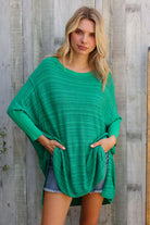Woman wearing a green oversized long sleeves top against a wooden background