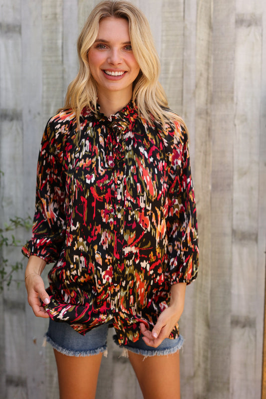 Woman wearing a colorful patterned blouse and denim shorts standing against a wooden fence.