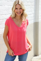 Woman wearing a pink top and blue jeans against a white brick wall.