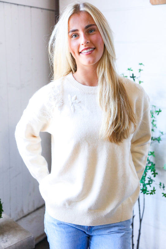 Woman wearing a cream sweater and blue jeans indoors with a plant in the background
