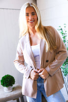 Woman wearing a beige blazer over a white top and blue jeans indoors.