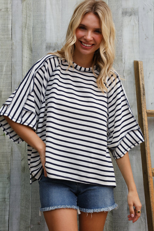 Woman wearing a black and white striped shirt and denim shorts standing against a wooden background