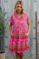 Woman wearing a bright pink floral dress against a wooden background