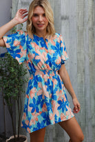 Woman wearing a colorful floral dress against a wooden wall.