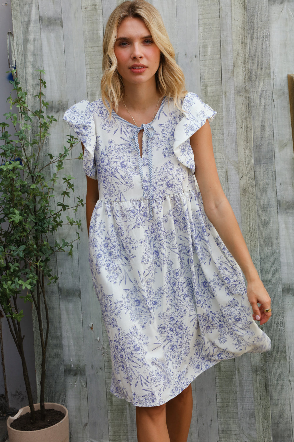 Woman wearing a white floral dress against a wooden wall.