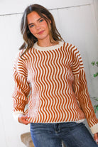 Woman wearing a burnt orange and white striped sweater with blue jeans against a white wall.