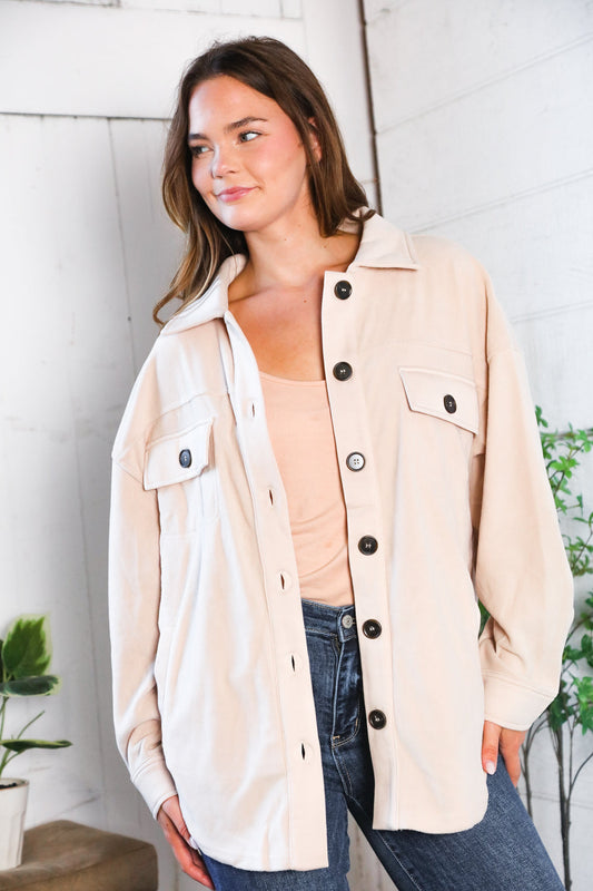 Woman wearing a beige Shacket shirt with black buttons indoors against a white wall.
