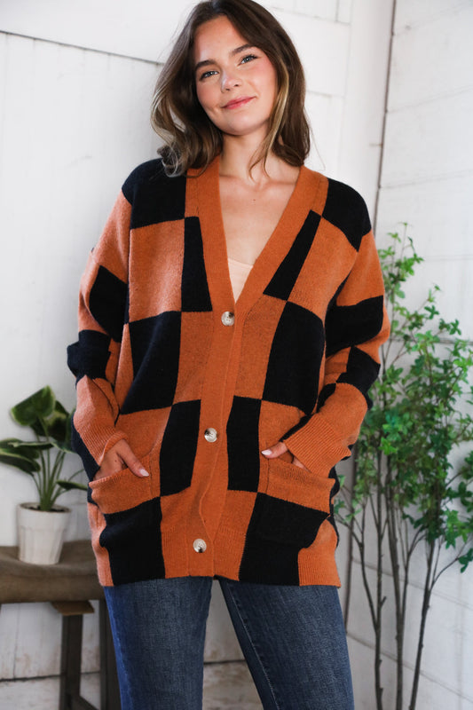 Woman wearing a patterned cardigan with a white brick wall and plants in the background