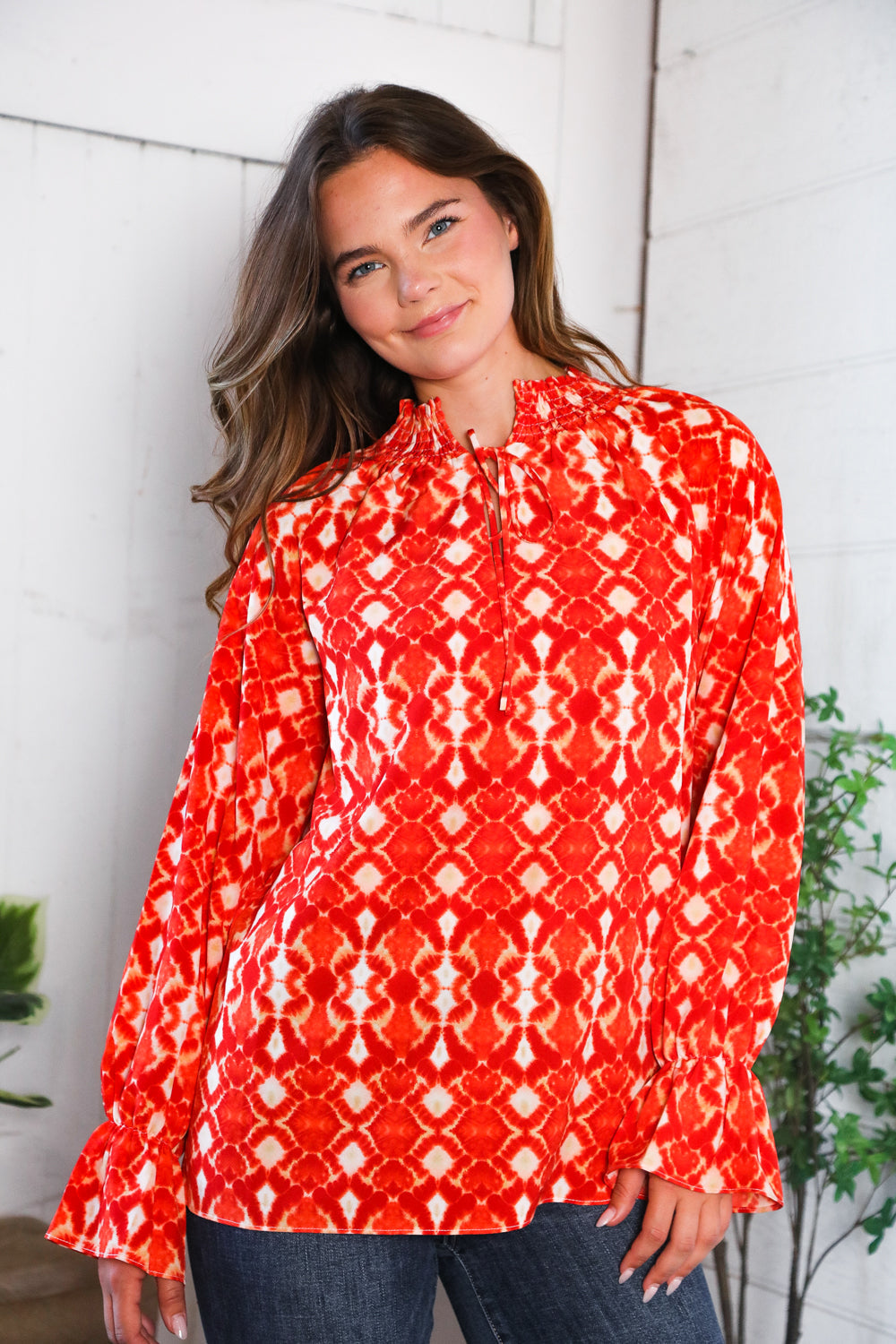 Woman wearing a red patterned blouse against a white wall.