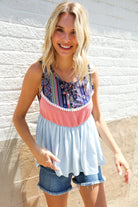 Woman wearing a colorful top and denim shorts against a textured wall.