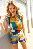 Woman wearing a colorful floral shirt top blouse against a white brick wall