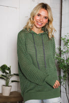 Woman wearing a green hoodie standing indoors with plants in the background