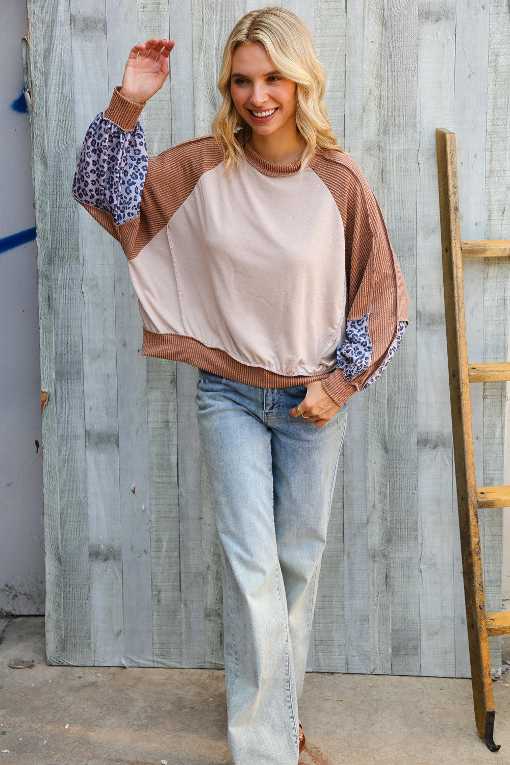 Woman wearing a brown, tan and animal print long sleeve shirt standing against a wooden wall.