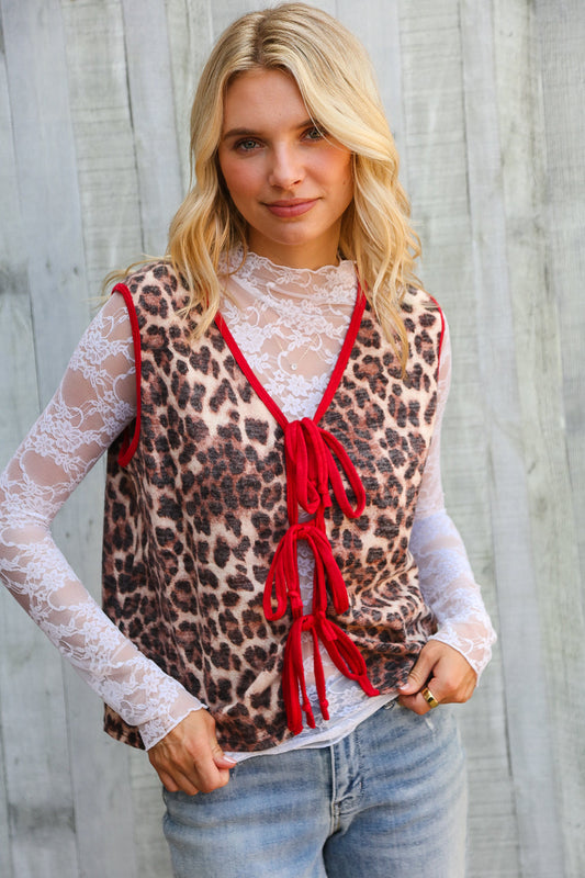 Woman wearing a leopard print vest with red accents and lace sleeves against a wooden background