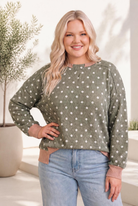 A cozy ribbed pullover in olive with white polka dots, mauve trim, and a relaxed fit, worn by a smiling model.