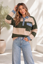 A woman wearing an olive and tan striped sweater with denim collar and cuffs, standing in a cozy room.