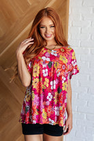 A woman wearing a pink floral top with a round neckline and short, flutter sleeves.